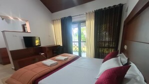 Ein Hotelzimmer mit Bett, Fernseher, Schreibtisch und einem Balkon mit Vorhängen.