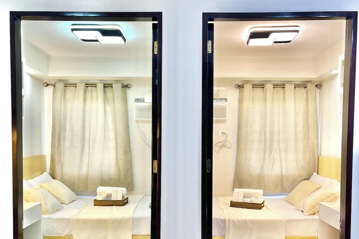 Habitación con espejo, dos camas, ventana con cortinas y suelo de baldosas.