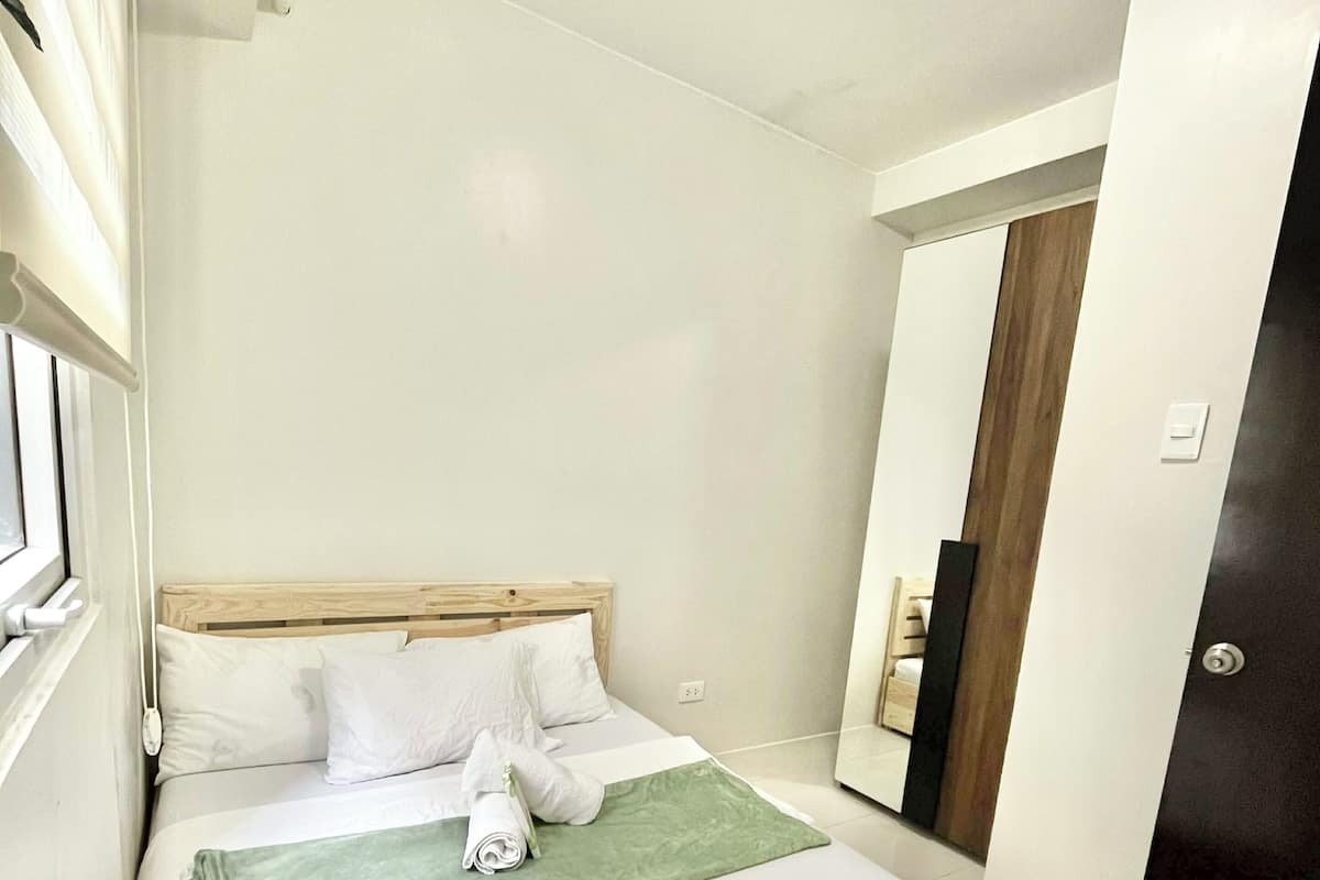 Una cama bien hecha con sábanas blancas, un edredón verde y una toalla enrollada al lado.