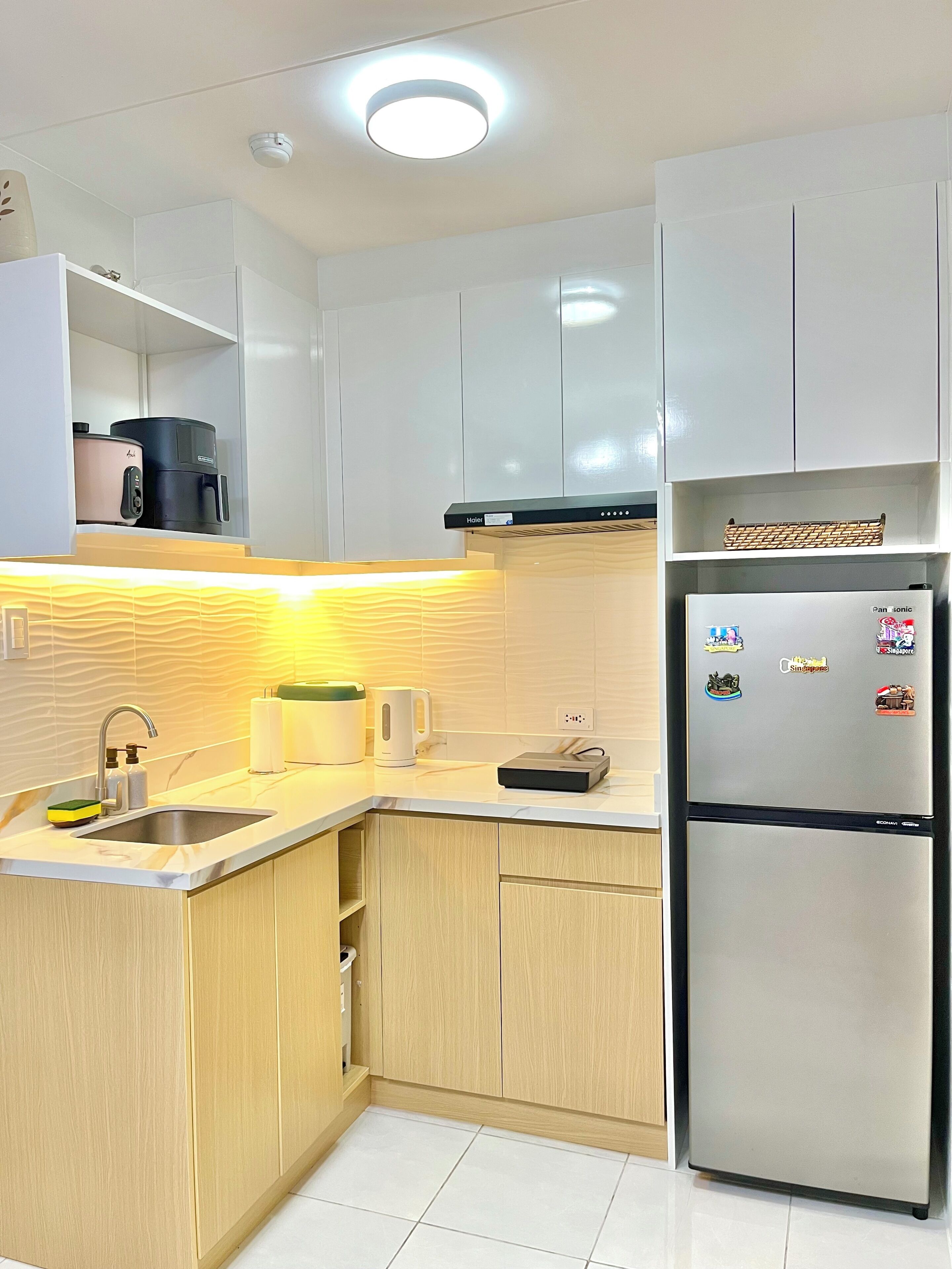 Eine moderne Küche mit weißen Schränken, einem Edelstahlkühlschrank, einem eingebauten Backofen und einem Spülbecken mit Armatur.