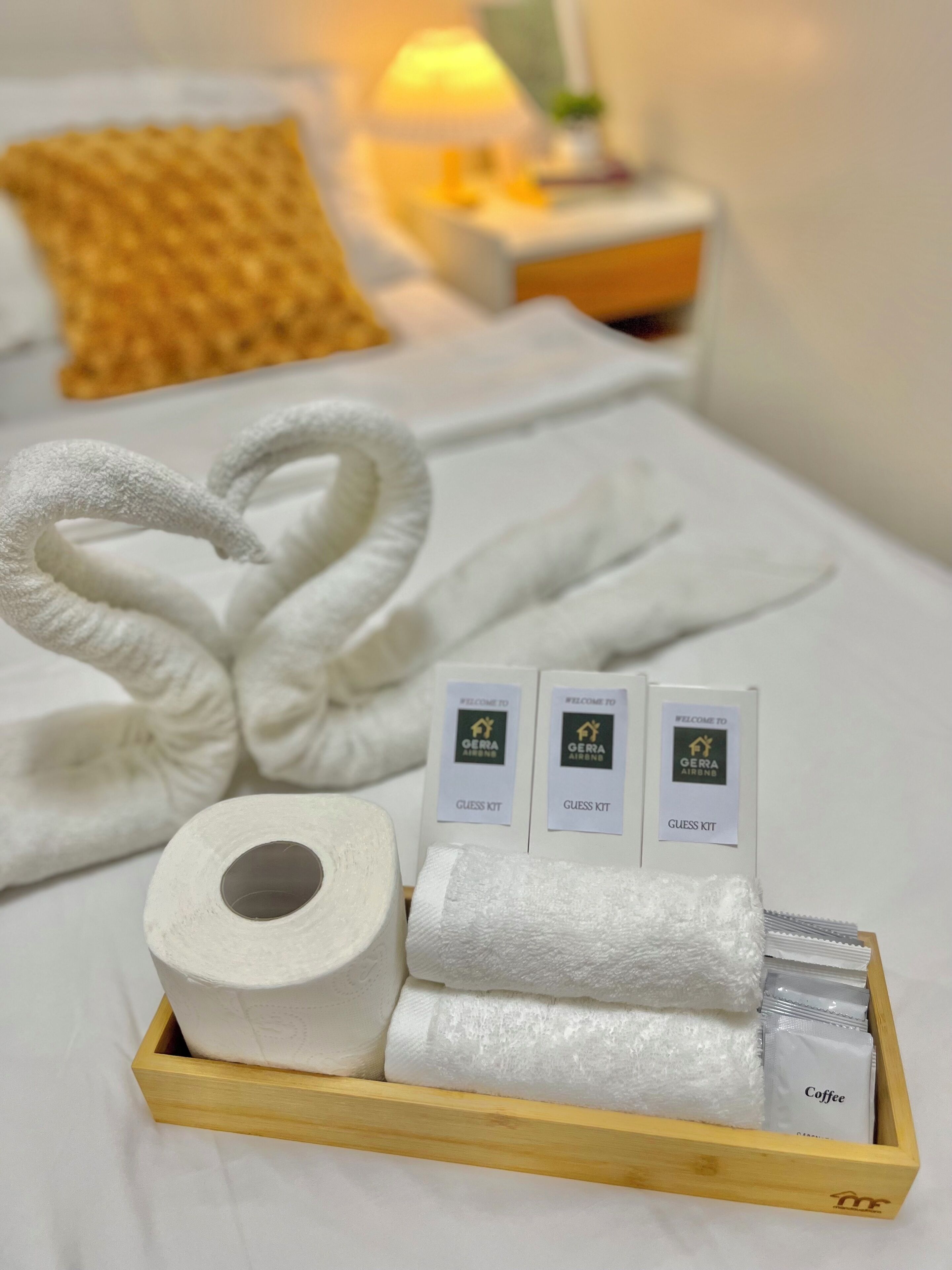 Une chambre d’hôtel bien rangée, avec un lit, un plateau en bois contenant des serviettes, un rouleau de papier toilette et un kit de bienvenue.