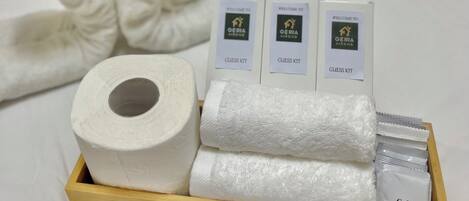 Une chambre d’hôtel bien rangée, avec un lit, un plateau en bois contenant des serviettes, un rouleau de papier toilette et un kit de bienvenue.