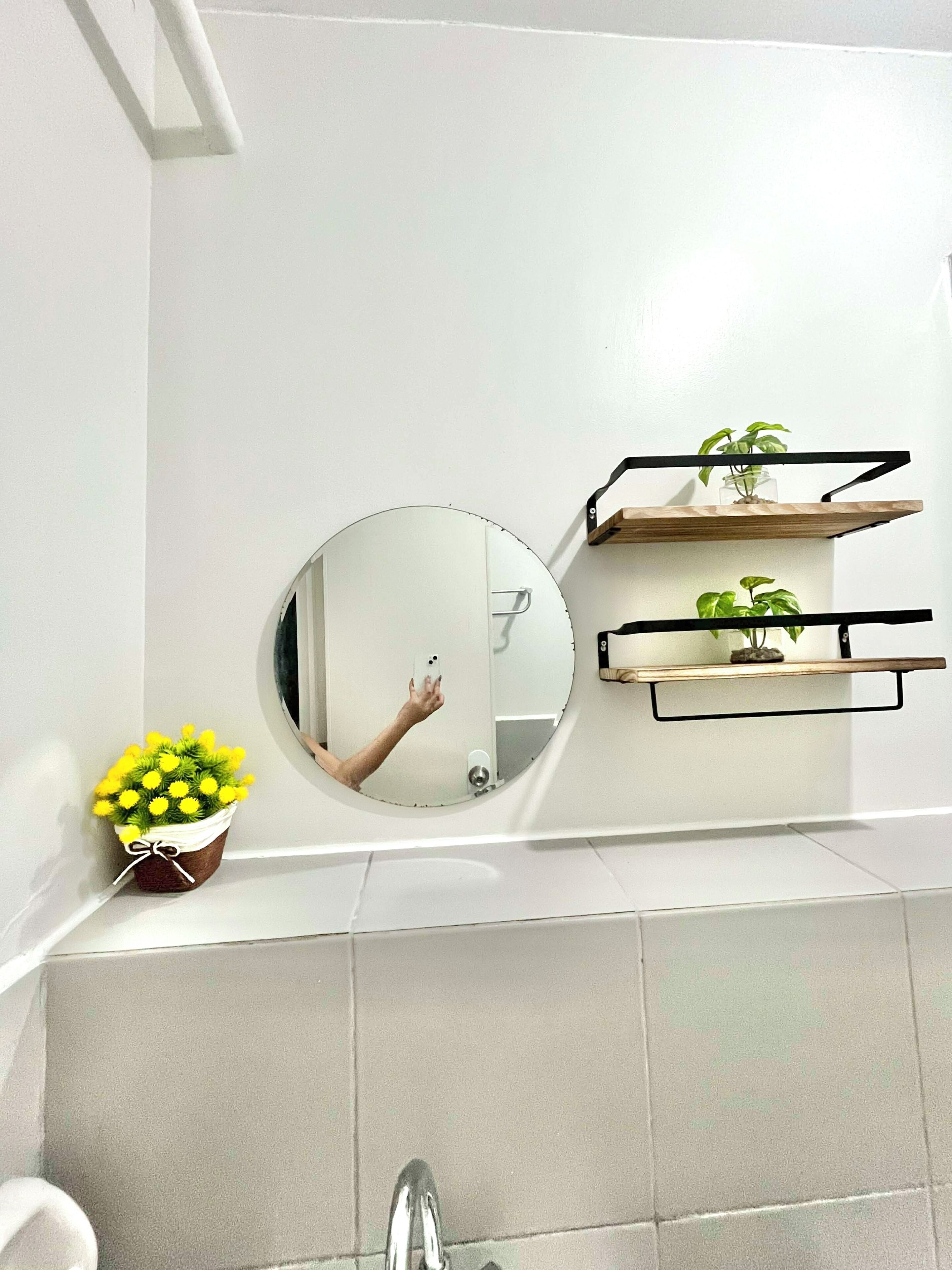 A bathroom with a round mirror, a small plant, and a shelf with another plant.