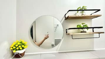 A bathroom with a round mirror, a small plant, and a shelf with another plant.