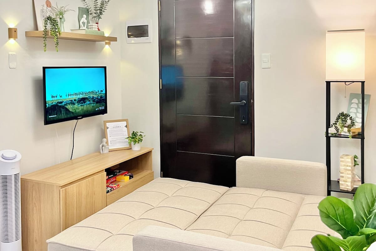 Una sala de estar moderna con una televisión de pantalla plana, un sofá, una mesa de centro, una lámpara de techo y una puerta.