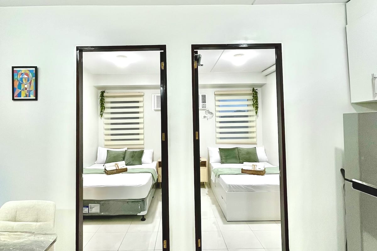 Una habitación moderna con dos camas, una silla blanca y una mesita pequeña.