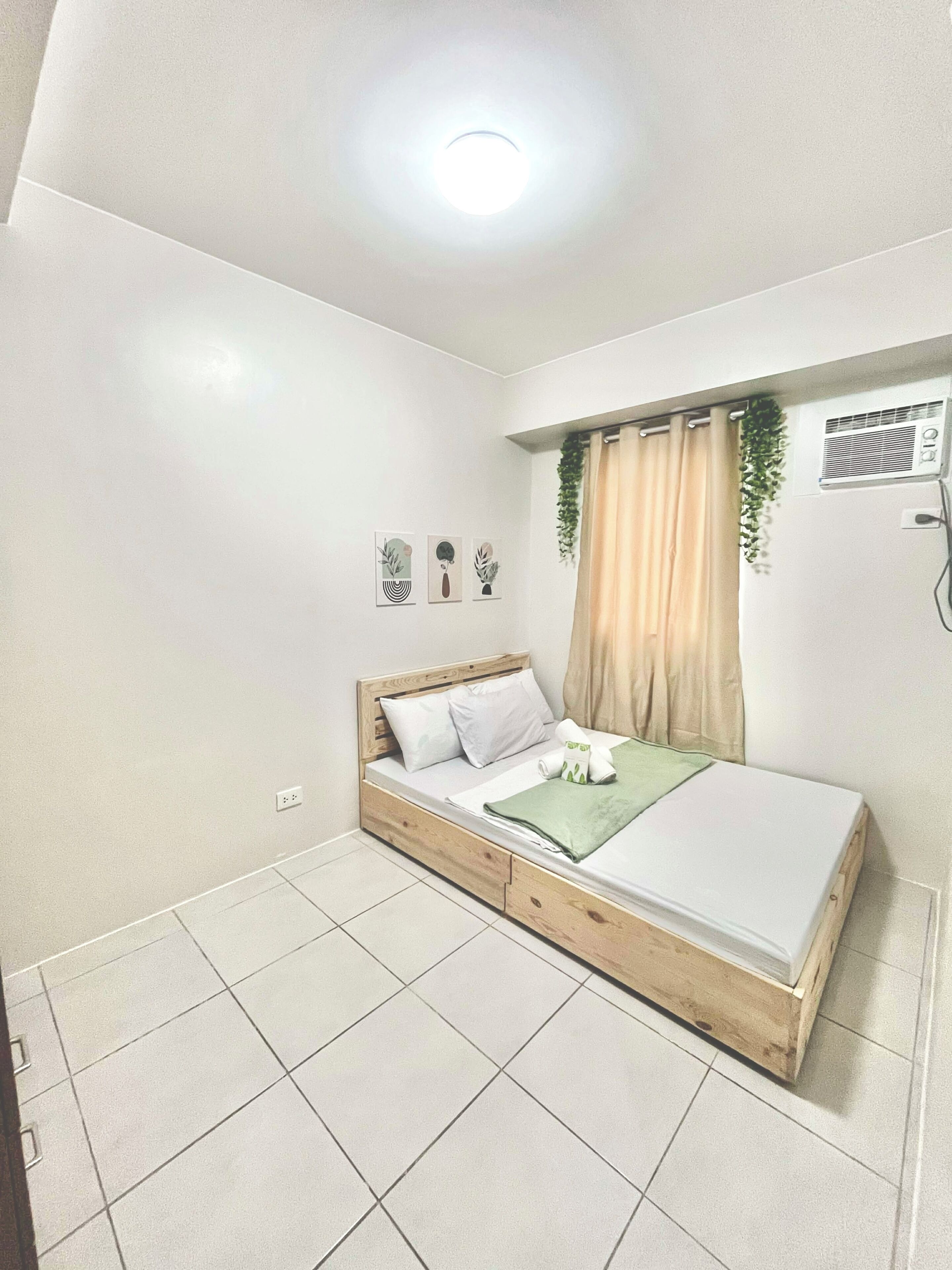 A bedroom with a bed, a ceiling light, a wall-mounted air conditioner, and a window with curtains.
