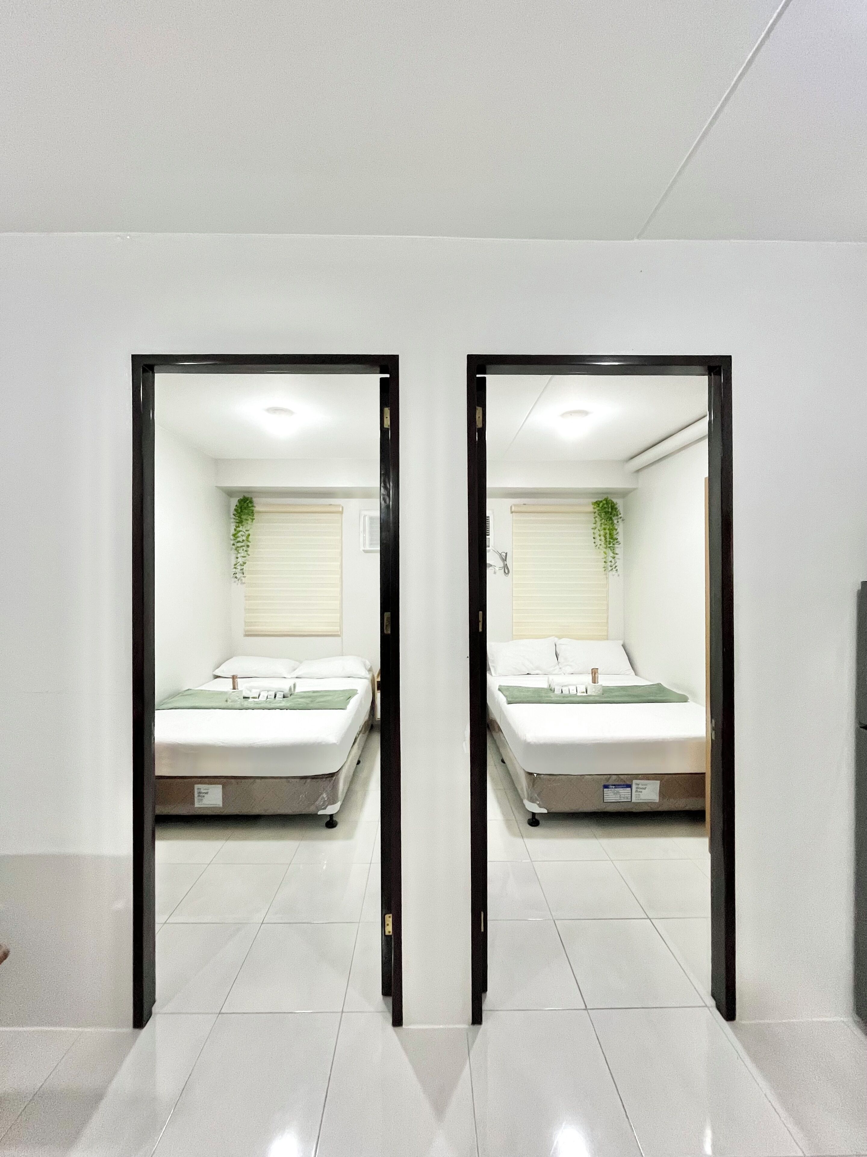 A mirrored room with a bed, a window with blinds, and a plant.