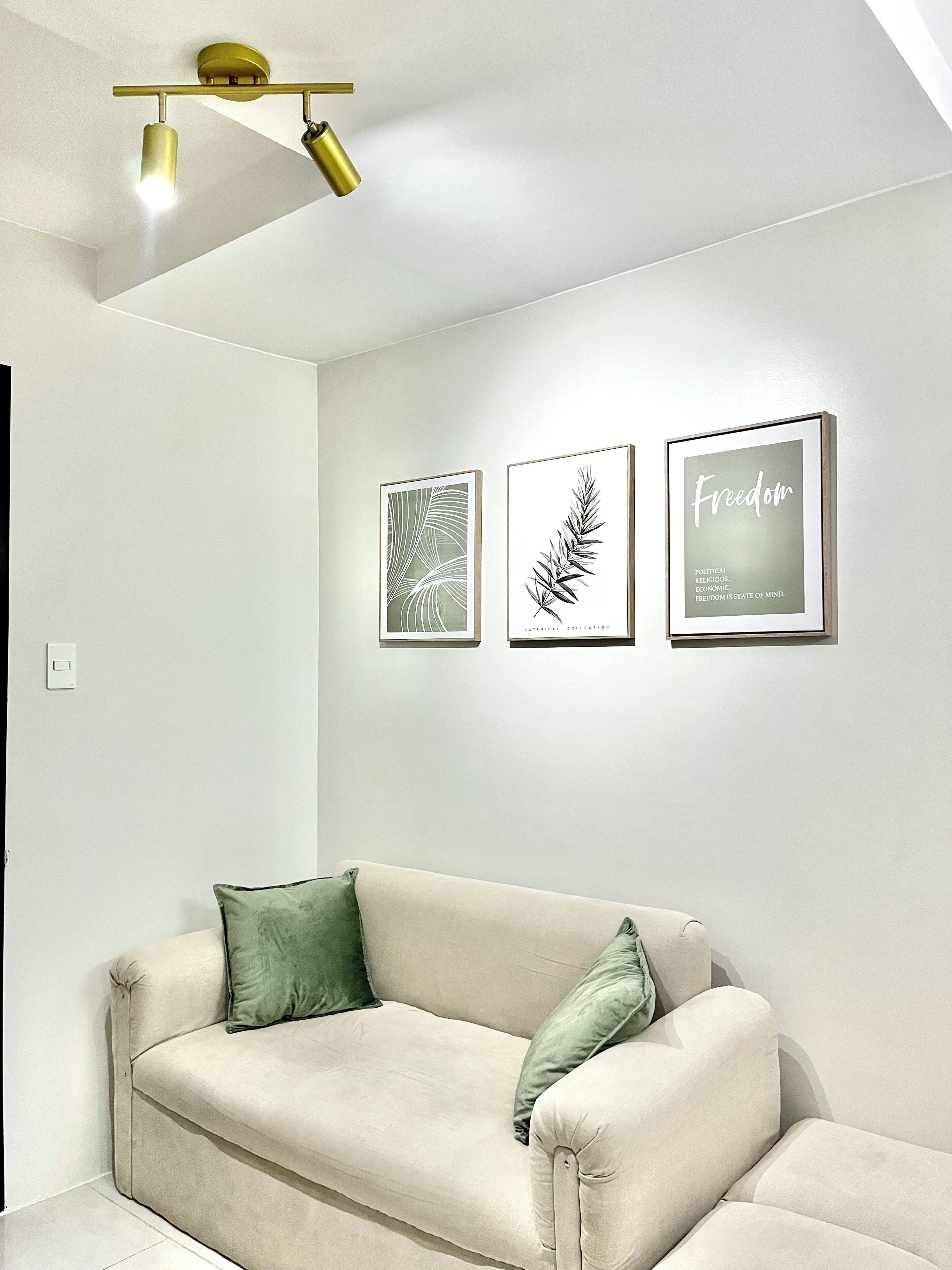 Un salon minimaliste avec un canapé beige, des coussins verts et trois reproductions botaniques encadrées accrochées au mur.