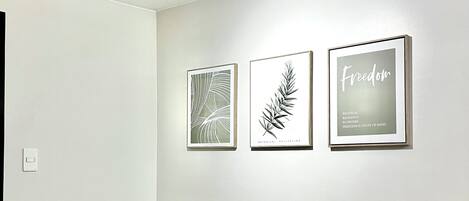 Un salon minimaliste avec un canapé beige, des coussins verts et trois reproductions botaniques encadrées accrochées au mur.