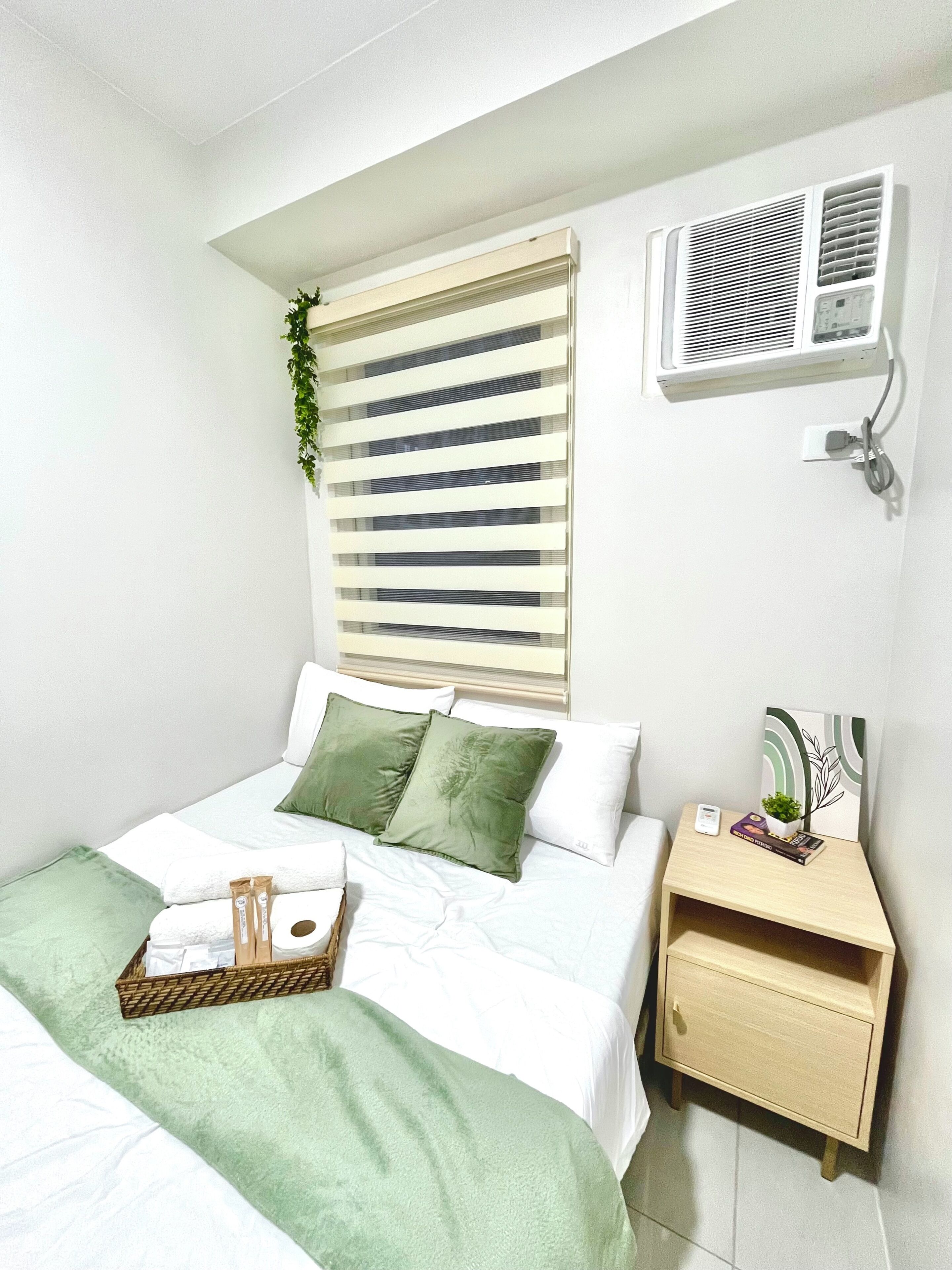 A neatly arranged bedroom with a bed, bedside table, and an air conditioning unit.