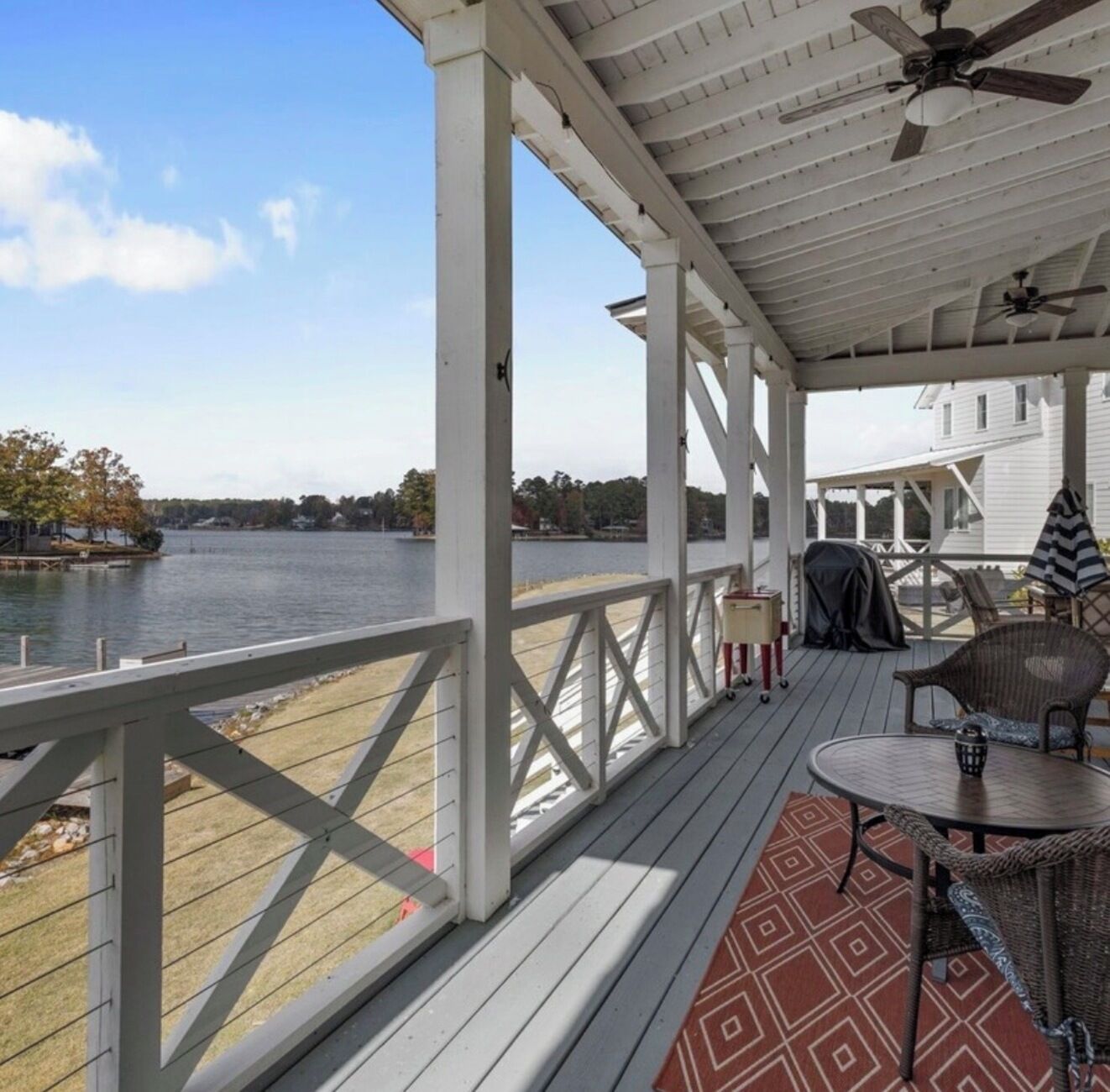 A covered deck with a view of a lake, outdoor furniture, and a ceiling fan.