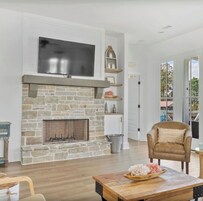 Una sala de estar con chimenea de piedra, un televisor montado y un sillón cómodo.