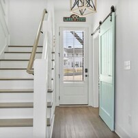 Una escalera conduce a una puerta con un cartel encima, una puerta azul claro, y se ve un paisaje a través del ventanal.