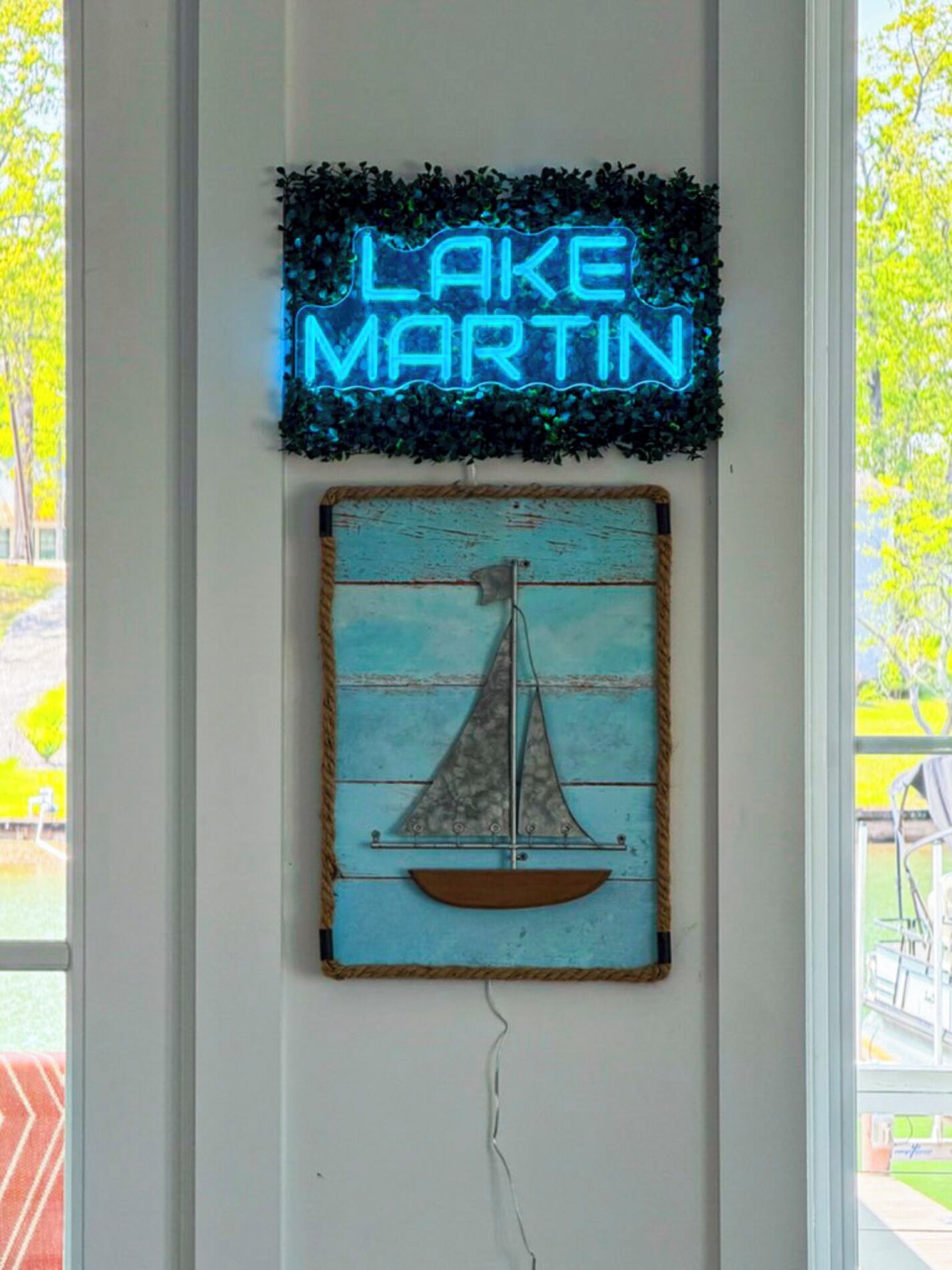 En neonskylt med texten ”LAKE MARTIN” och en rustik segelbåtsdekoration på en vägg.