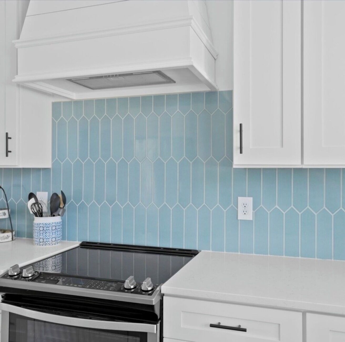 A kitchen with white cabinets, a blue-tiled backsplash, and a stove.