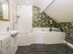 Ein Badezimmer mit einem weißen Waschbecken, einer Badewanne und einer Dusche. Die Wand ist mit strukturiertem Wandpapier versehen und auf dem Boden liegt ein kleiner Teppich.