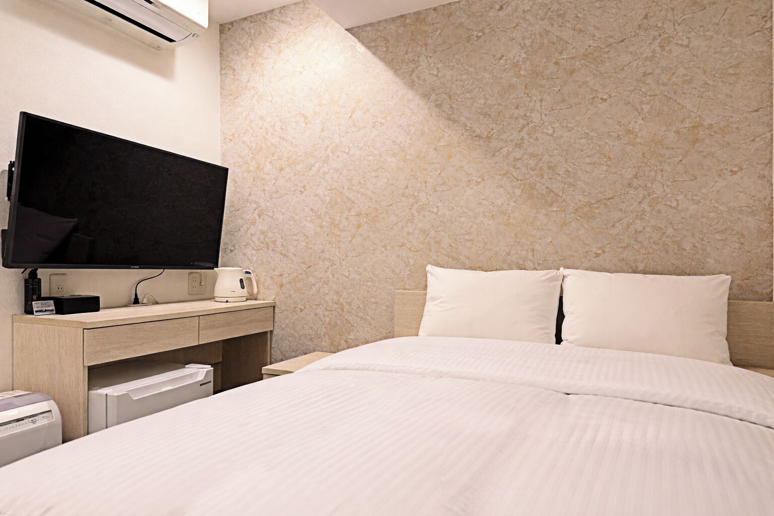 A hotel room with a bed, a flat-screen TV, a desk with a kettle, and a coffee machine.