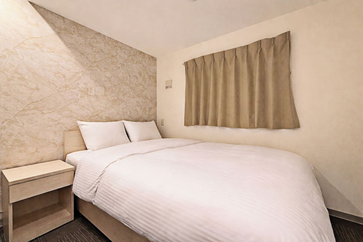 A hotel room with a bed, a nightstand, a marble wall, and a window with curtains.