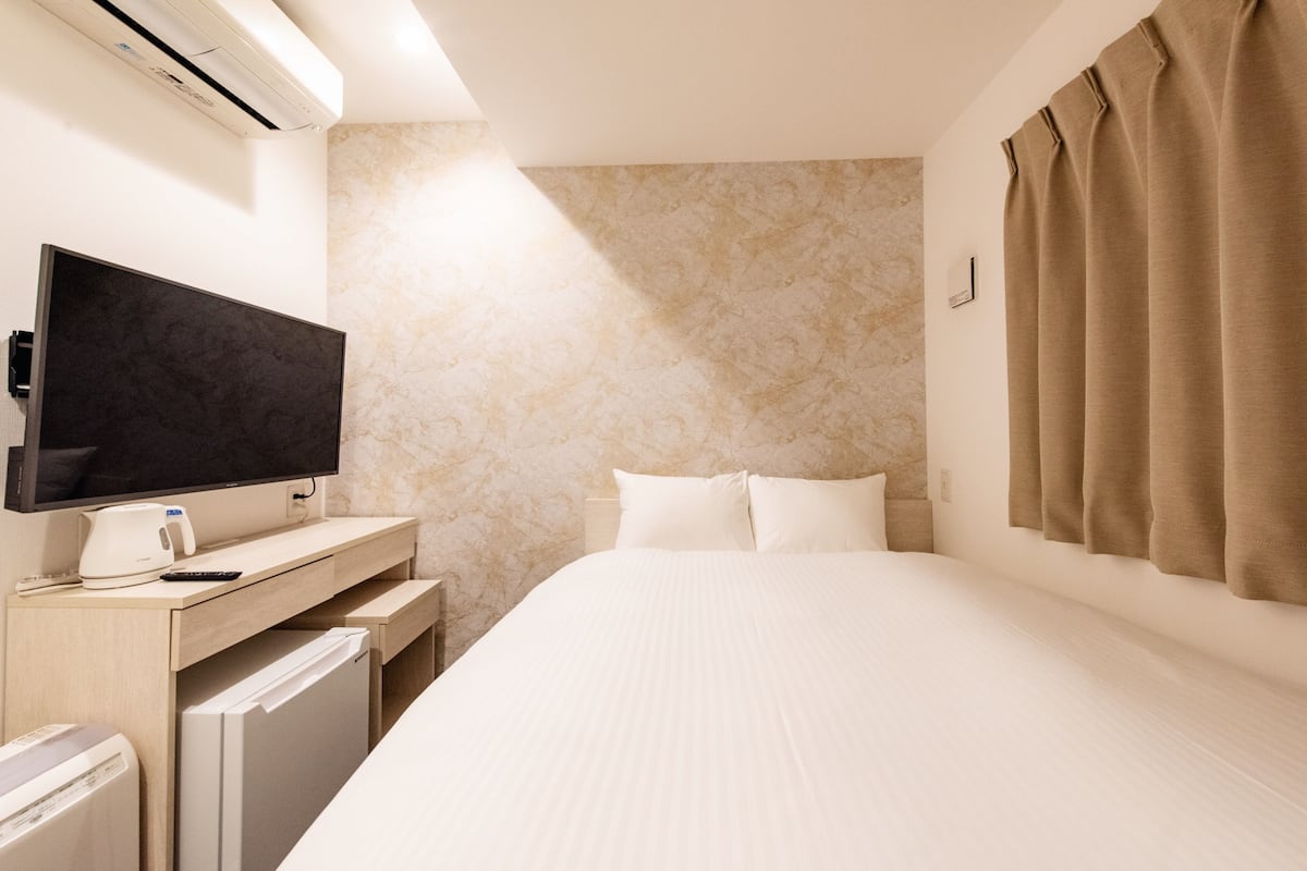 A hotel room with a bed, a TV, a desk with a coffee maker, and an air conditioner.