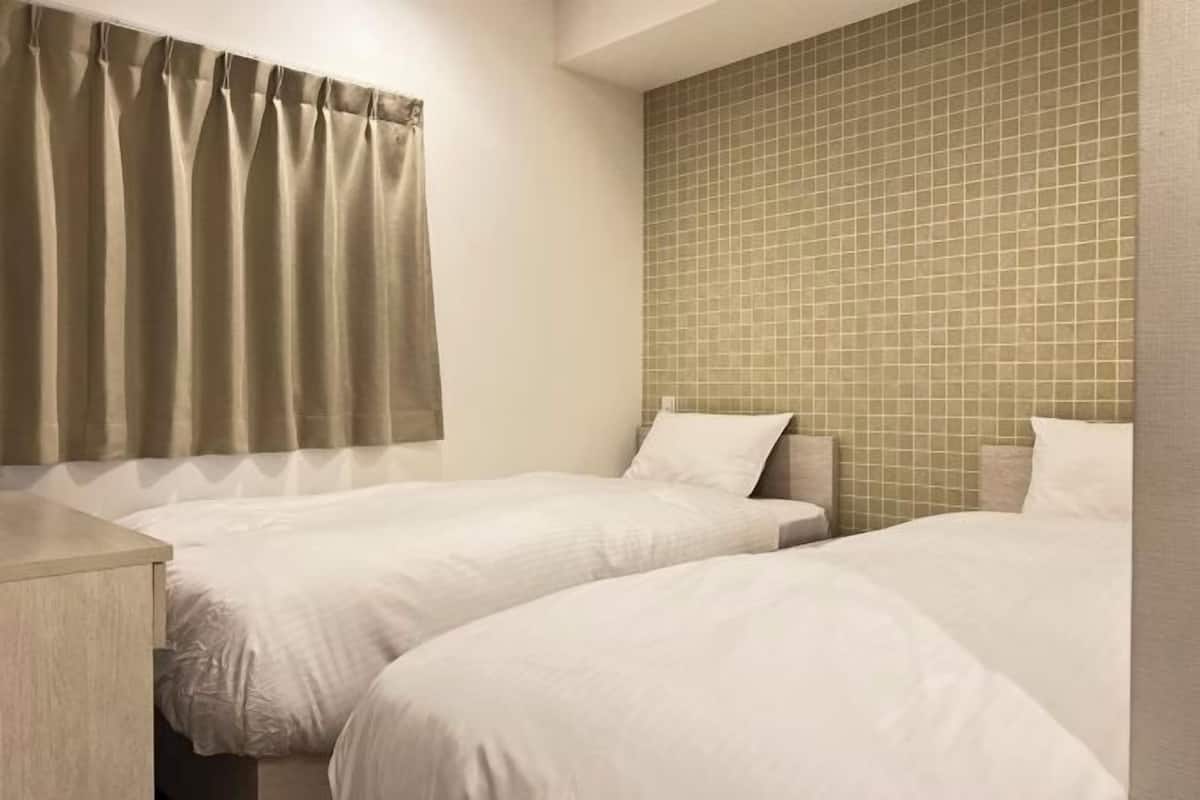 A hotel room with two beds, a nightstand, and a tiled wall.