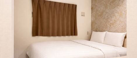 Una habitación de hotel con cama, mesita de noche, lámpara de pared y cortina.