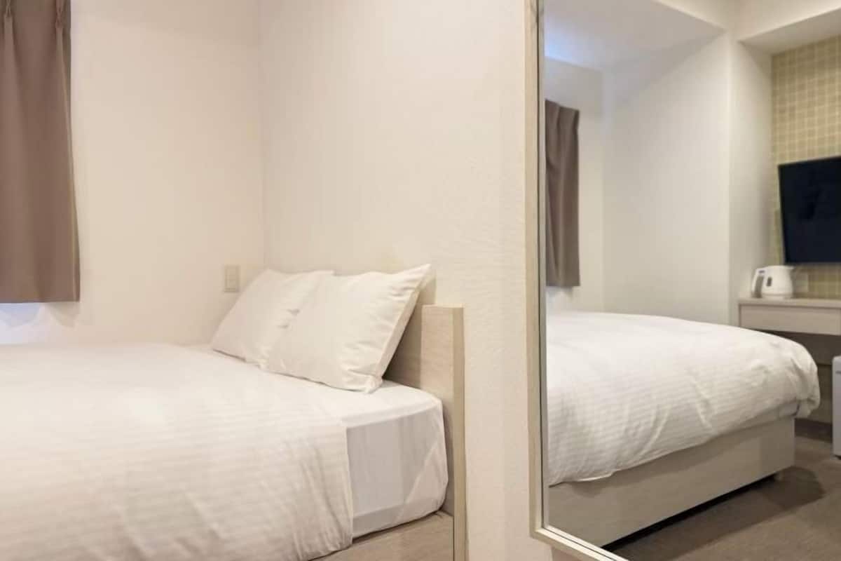 A hotel room with two beds, a mirror, a television, and a small table with a kettle.