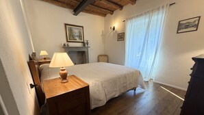 Une chambre à coucher avec un lit, une table de chevet en bois surmontée d’une lampe, une cheminée et une fenêtre avec des rideaux.