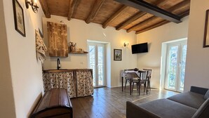 Un salon chaleureux avec un plafond en bois, une table à manger avec des chaises, un canapé et un téléviseur fixé au mur.