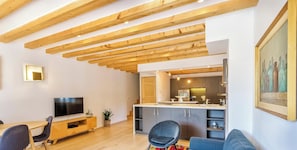 Ein moderner Wohnraum mit freiliegenden Holzbalken, einem Flachbildfernseher, einem Essbereich, einer Küche und einem Sofa.