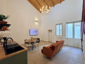 A modern kitchen with a sink, dining area, and a sofa. There is a chandelier, a wall-mounted TV, and a door leading to a balcony. - Isula Antica (Floridia)
