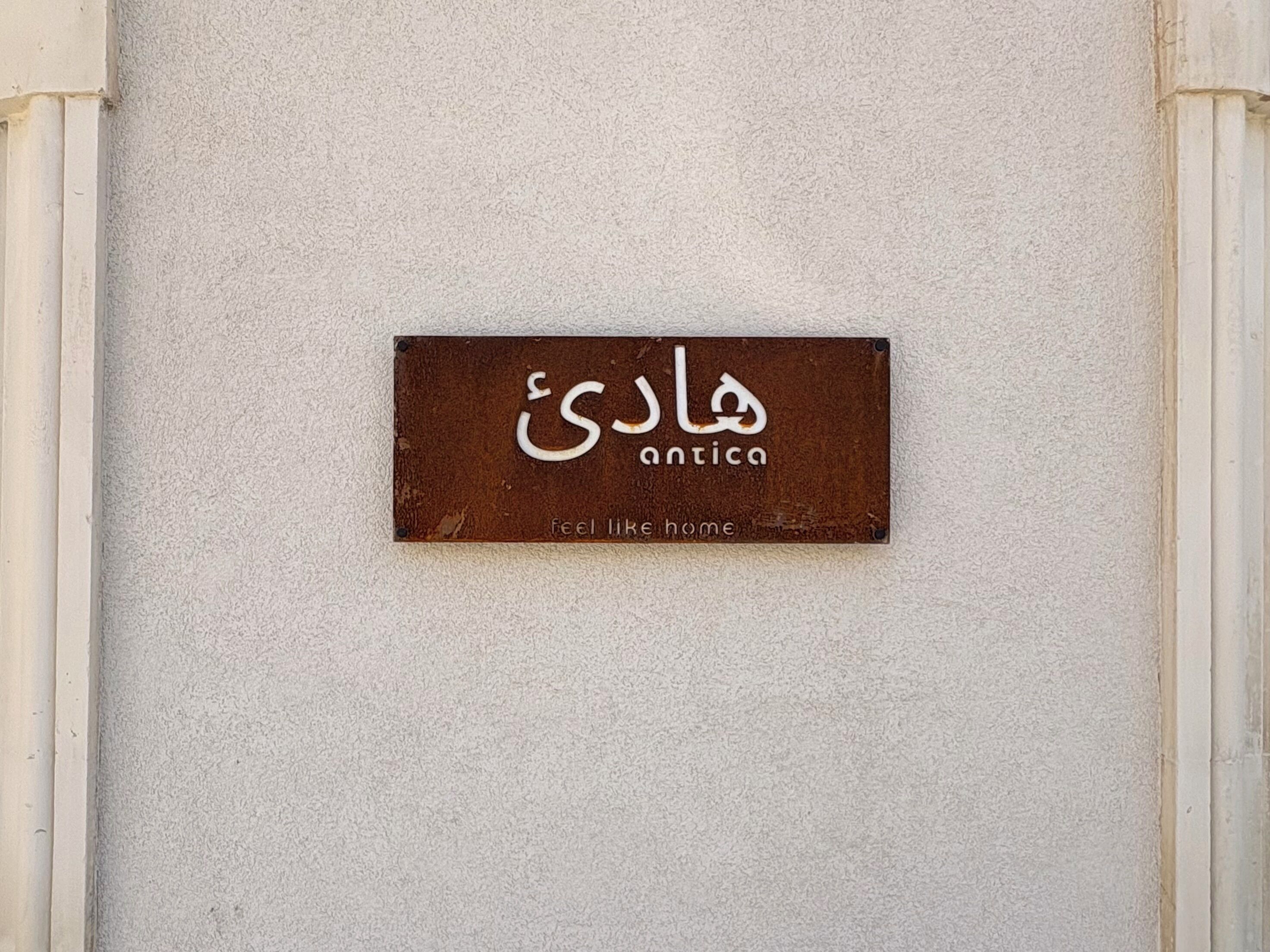 A sign with the word 'antica' and the phrase 'feel like home' on a textured wall.
