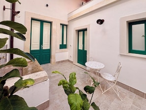 A courtyard with a white tiled floor, green doors, a round table with chairs, and potted plants. - Isula Antica (Floridia)