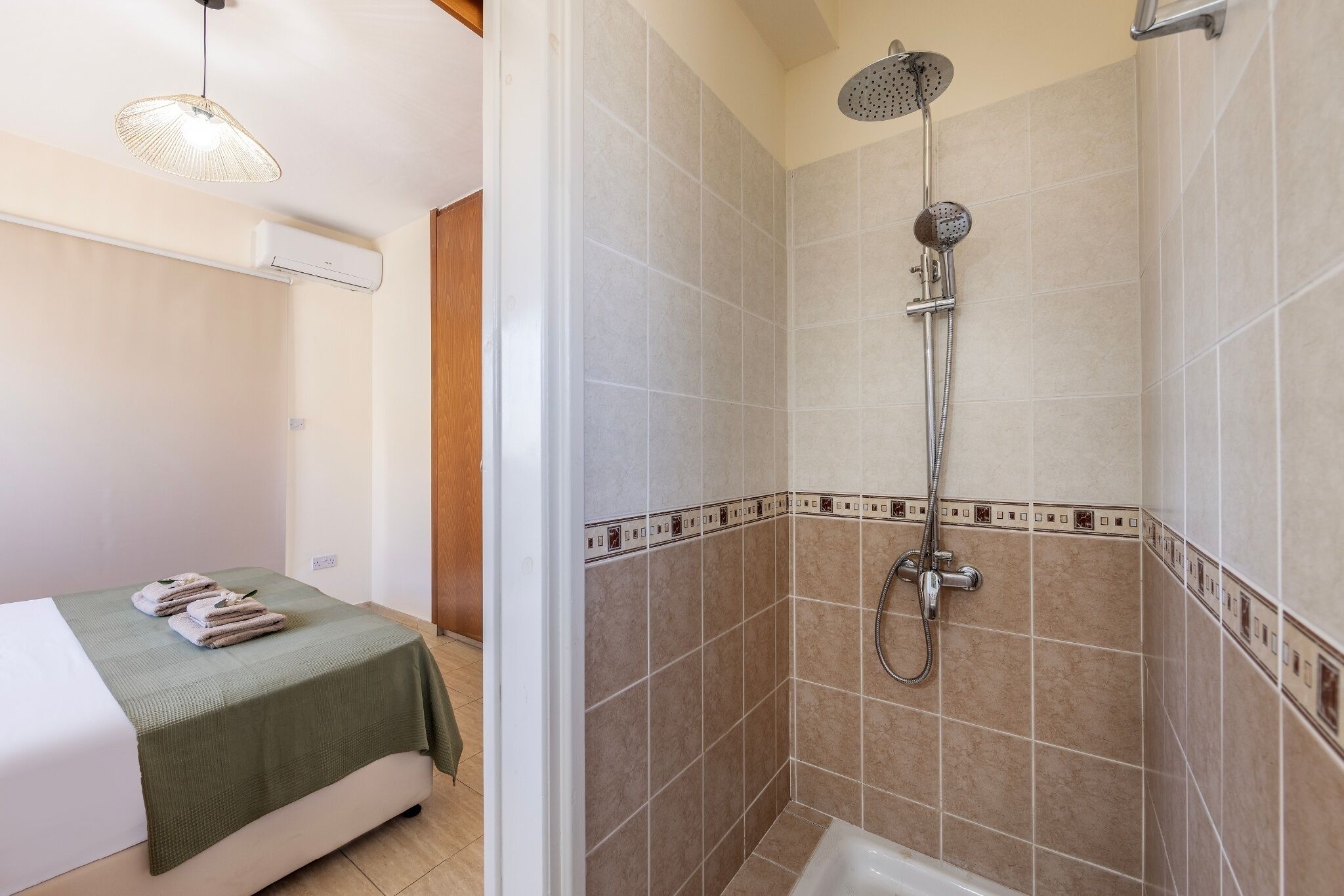 A bathroom with a shower, a bed with a green bedspread, and a hanging light fixture.