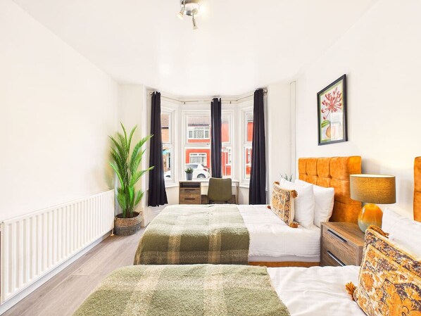 A bedroom with a bed, bedside table, lamp, and a view of a street through a window.