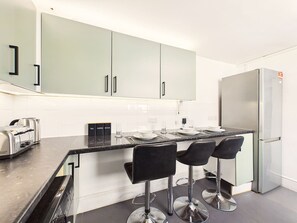Eine moderne Küche mit einer zentralen Kochinsel, Barhocker, einem Edelstahlkühlschrank und einem Toaster.