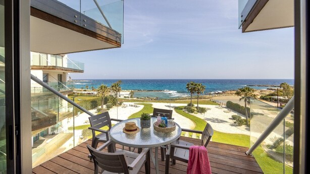 Ein Balkon mit Tisch, Stühlen und Blick auf den Ozean und den Strand.