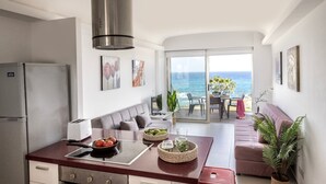 Eine moderne Küche mit Meerblick, ein Essbereich mit Tisch und Stühlen sowie ein Wohnbereich mit einer Couch und Pflanzen.