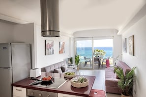 Eine moderne Küche mit Meerblick, ein Essbereich mit Tisch und Stühlen sowie ein Wohnbereich mit einer Couch und Pflanzen.
