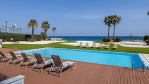 A pool with lounge chairs, palm trees, and a view of the ocean. - 1 bedroom apartment in Protaras (Paralimni)