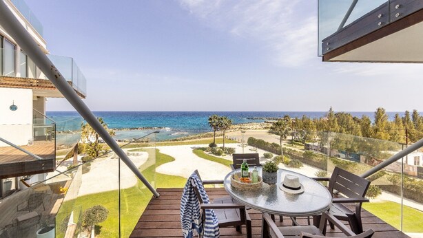 A balcony with a table, chairs, and a view of the ocean and golf course. - 1 bedroom apartment in Protaras (Paralimni)