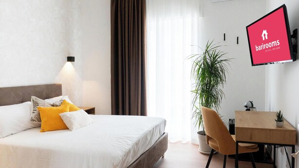 A hotel room with a bed, a desk, a chair, a potted plant, and a TV screen displaying 'bathrooms'. - Barirooms - Cardassi Suites (Bari)