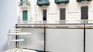 A balcony with a white table and chairs, a metal grill, and a building with green shutters and balconies. - Barirooms - Cardassi Suites (Bari)