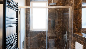A glass-enclosed shower with a handheld showerhead, a towel rack, and a marble-tiled wall. - Barirooms - Cardassi Suites (Bari)