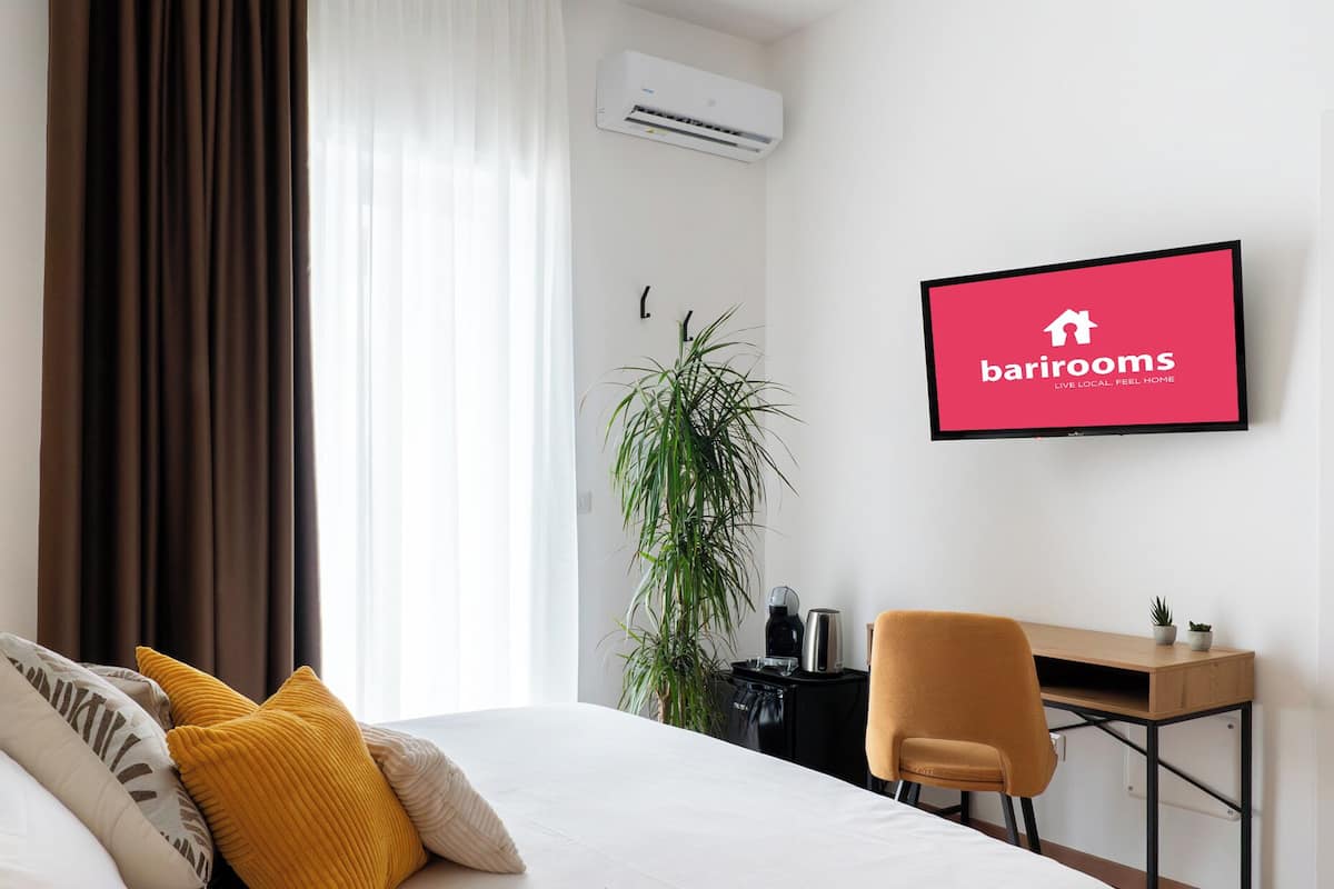 Una habitación de hotel con cama, escritorio, silla, aire acondicionado y un cartel enmarcado en la pared.