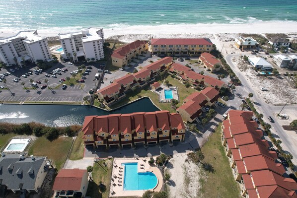 Vista aerea di un complesso alberghiero costiero con diversi edifici, una piscina e una spiaggia.