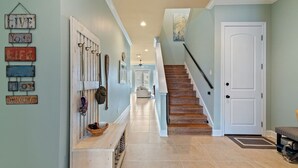A hallway with a wooden staircase, a white door, and a wall with decorative signs. - Spacious 4bedroom 3bathroom townhouse casual elegance w/ lagoon views! 2 Pools! (Pensacola Beach)