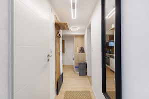 A narrow hallway with a wooden door, a small kitchen area with a microwave, and a trash bin.