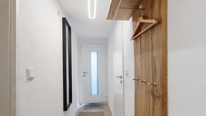Un pasillo con puerta de madera, pared blanca y una puerta con panel de vidrio esmerilado, además de una pequeña alfombra.