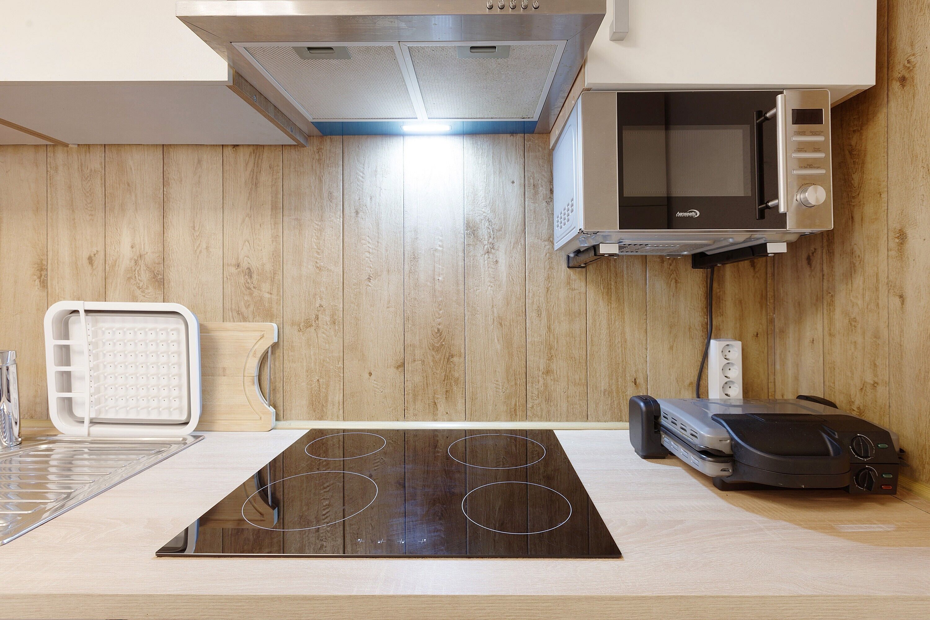 A kitchen with a built-in microwave, an induction cooktop, a toaster, and a kettle.